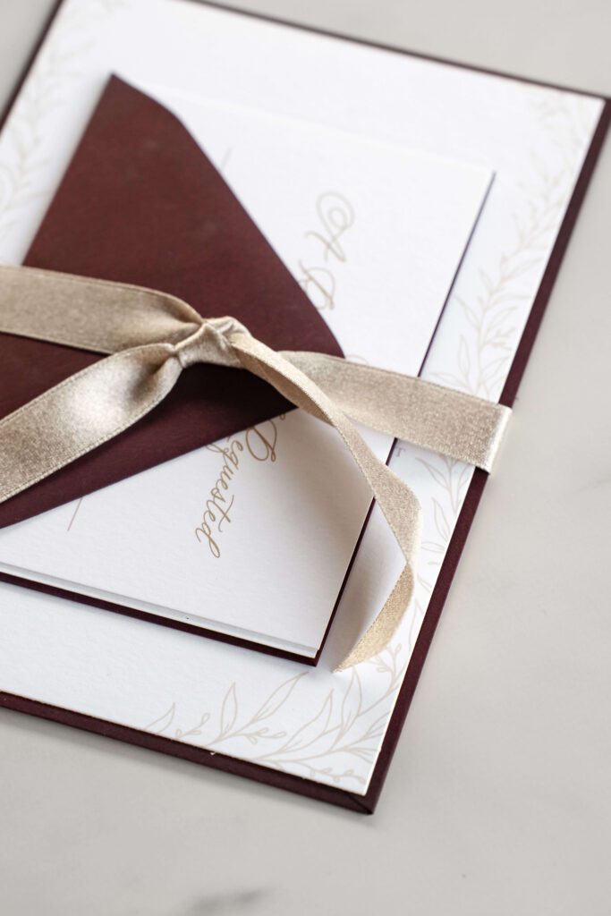 Luxe burgundy wedding invitation tied together by a champagne ribbon