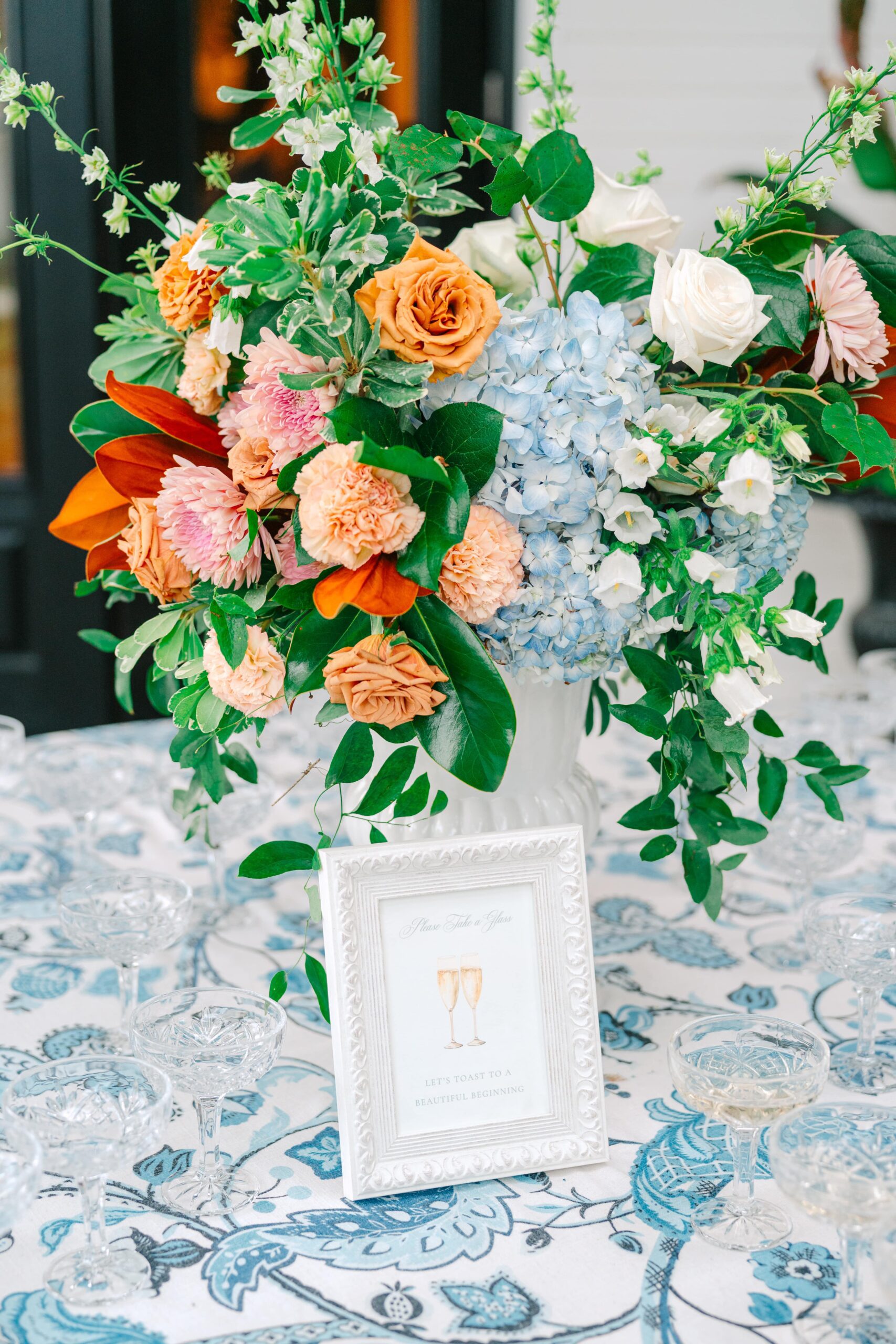 Champagne welcome table for a wedding reception with a sign that says "Please take a glass. Let's toast to a beautiful beginning."