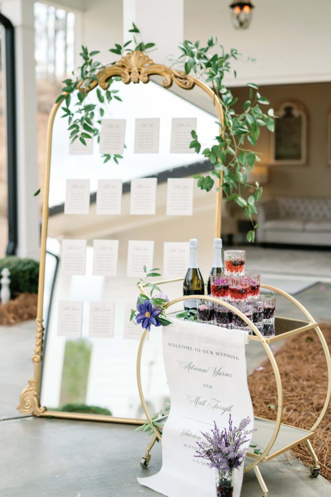 Escort card mirror display next to fabric wedding welcome sign displayed on bar cart