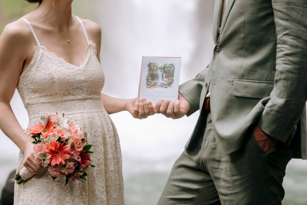 Bride and groom hold an elopement announcement card featuring a watercolor Costa Rica waterfall