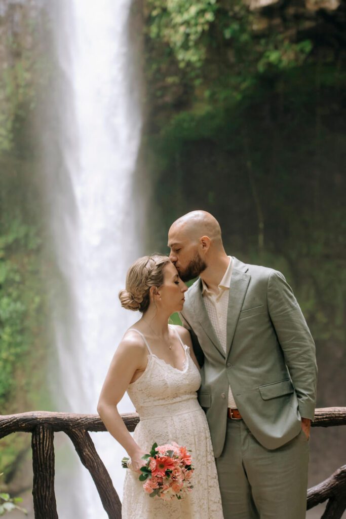 Groom kisses bride on the day of their elopement in front of La Fortuna Waterfall in Costa Rica