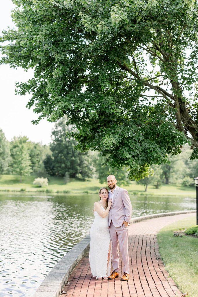 Bride and groom pose outdoors by a pond surrounded by lush greenery on their wedding day