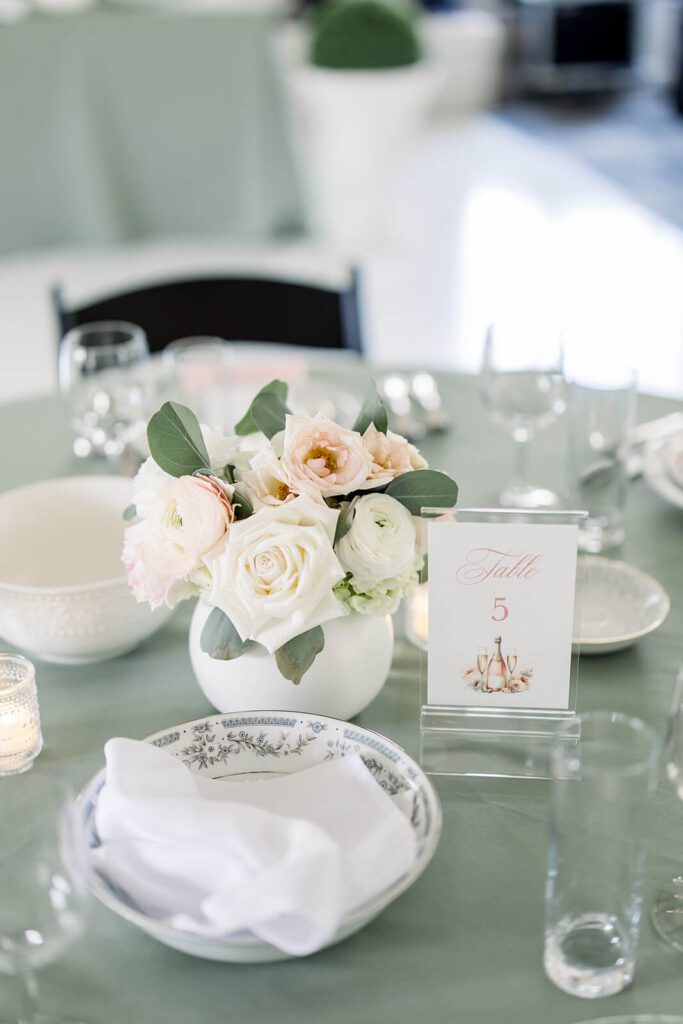 Sage green wedding reception table with elegant table number sign and roses
