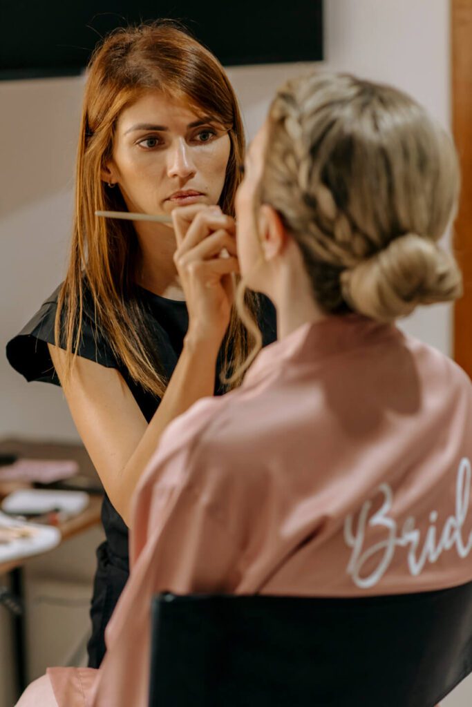 Makeup artist putting on bride's lipstick for her elopement