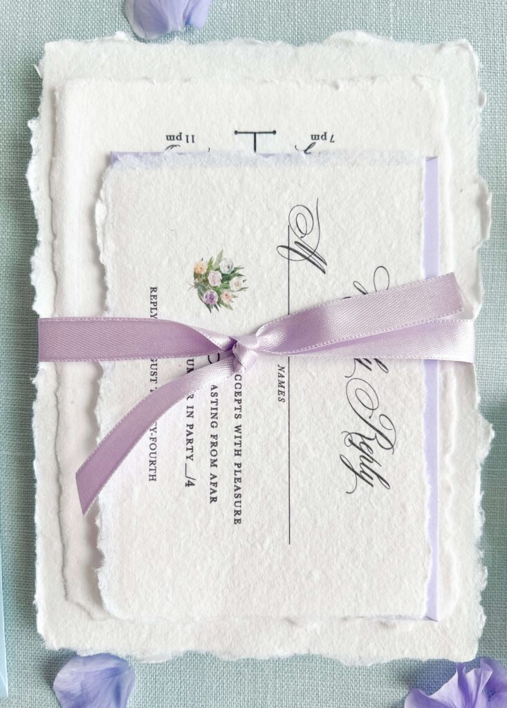 Whimsical garden wedding invitation suite on handmade paper with deckled edges, wrapped in a purple bow