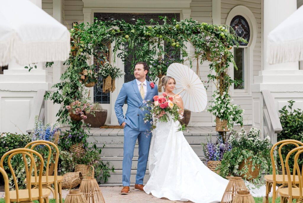 Bride and groom in front of whimsical ceremony arch on the front steps of The Grand Lady