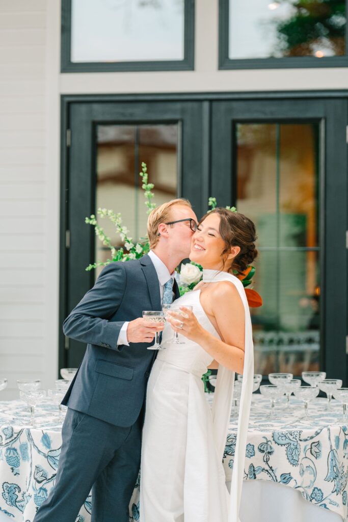 Groom kissing bride during champagne toast outside 1840 Manor House