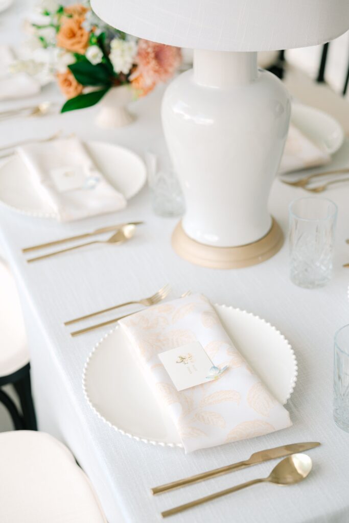 Elegant ivory and tan wedding reception table with elegant watercolor place card and gold cutlery