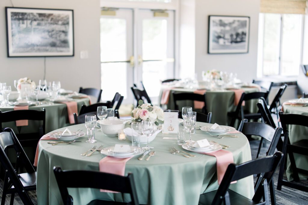Wedding reception tables with green tablecloths, pink napkins, and light pink floral centerpieces