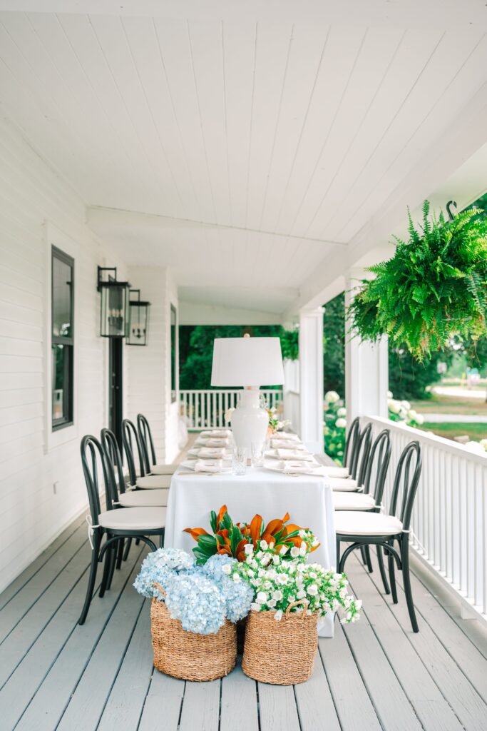 Ivory tablescape on the porch of 1840 Manor House, decorated with baskets of blue and white flowers