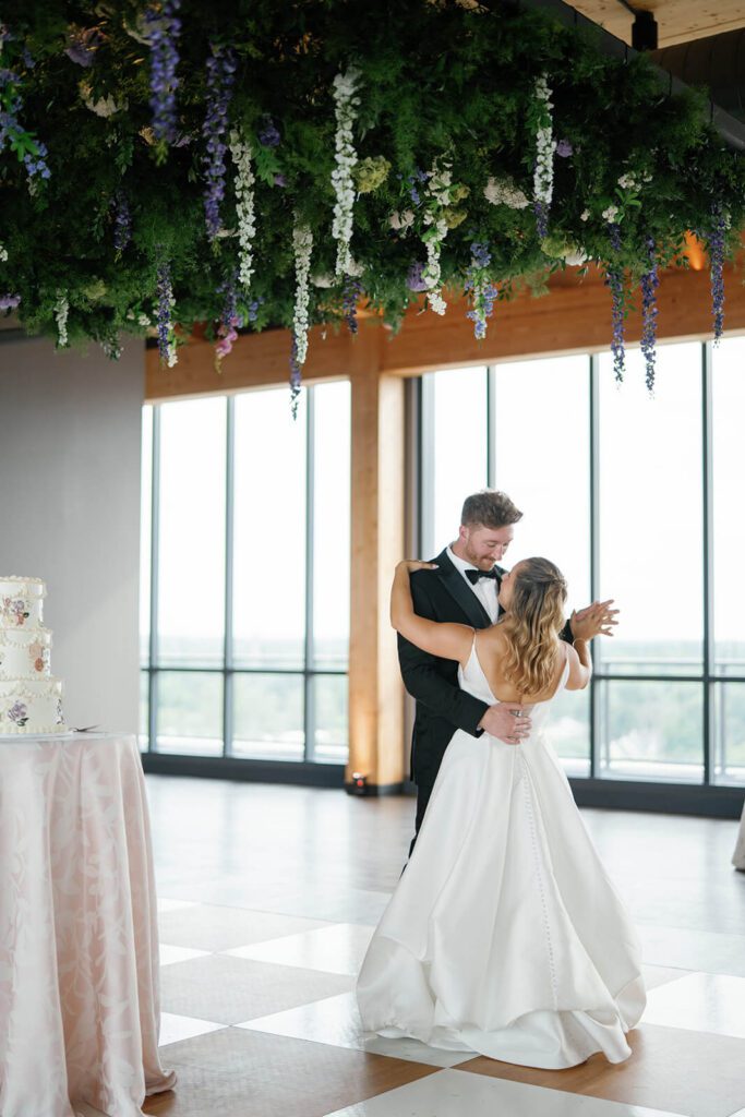 Bride and groom dancing on a checkered dance floor with a lush floral installation above