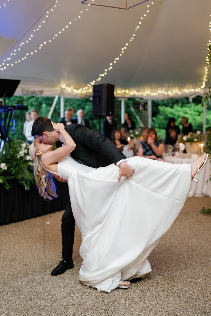 Groom dips bride on the dance floor and kisses her while guests cheer and smile