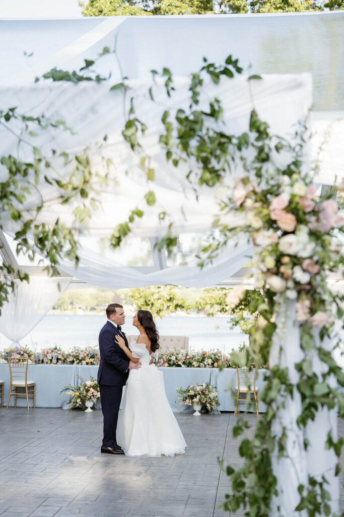 Bride and groom slow dance under their wedding reception tent, surrounded by greenery and white draping