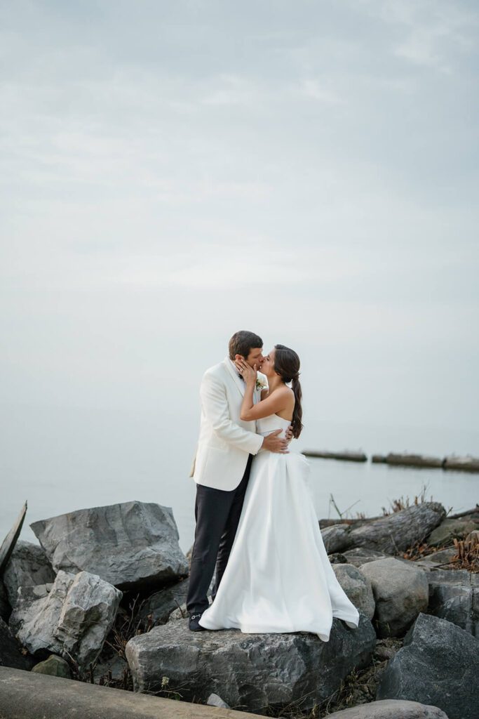 Bride and groom kiss on the rocks outside the Shoreby Club in Ohio