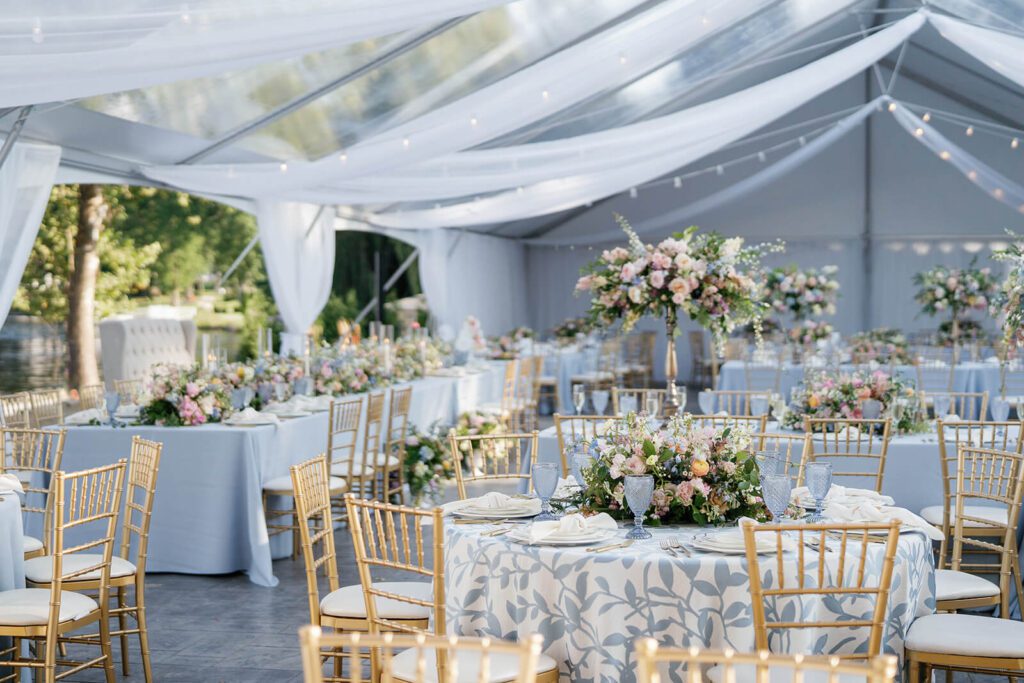 Romantic and elegant wedding reception tent with blue and white table decor, pastel florals, and white draping