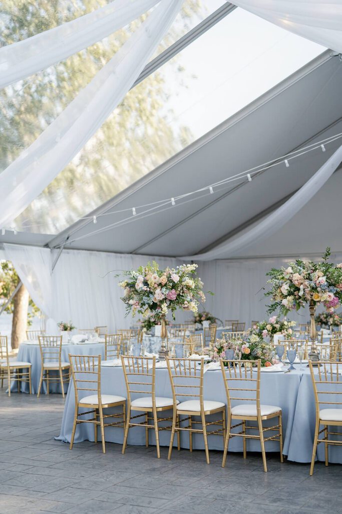 Elegant tented wedding reception with pastel florals and gold Chiavari chairs