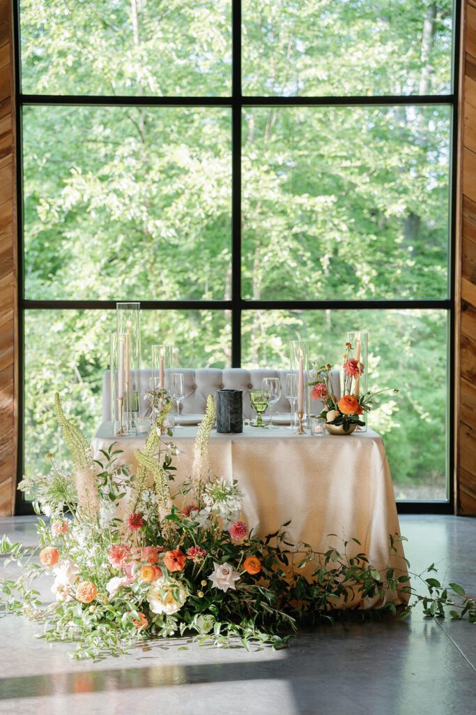Rustic and whimsical wedding sweetheart table in front of picturesque floor to ceiling windows