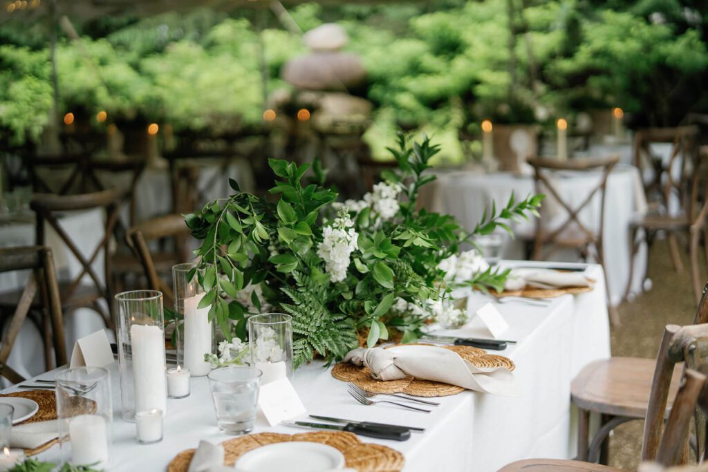 Rustic and elegant wedding reception table with greenery, wood chairs, and white pillar candles
