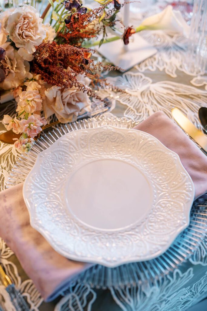 Intricate white china on top of a ribbed glass charger at a wedding reception