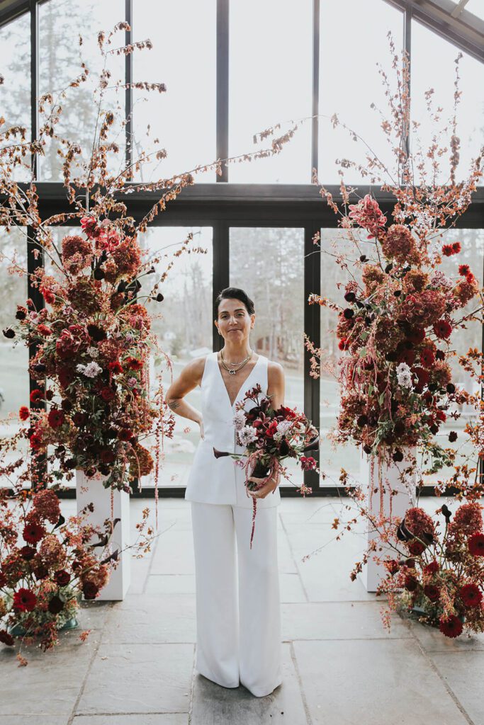 Bride wearing modern sleeveless pantsuit and holding a romantic bouquet in shades of red