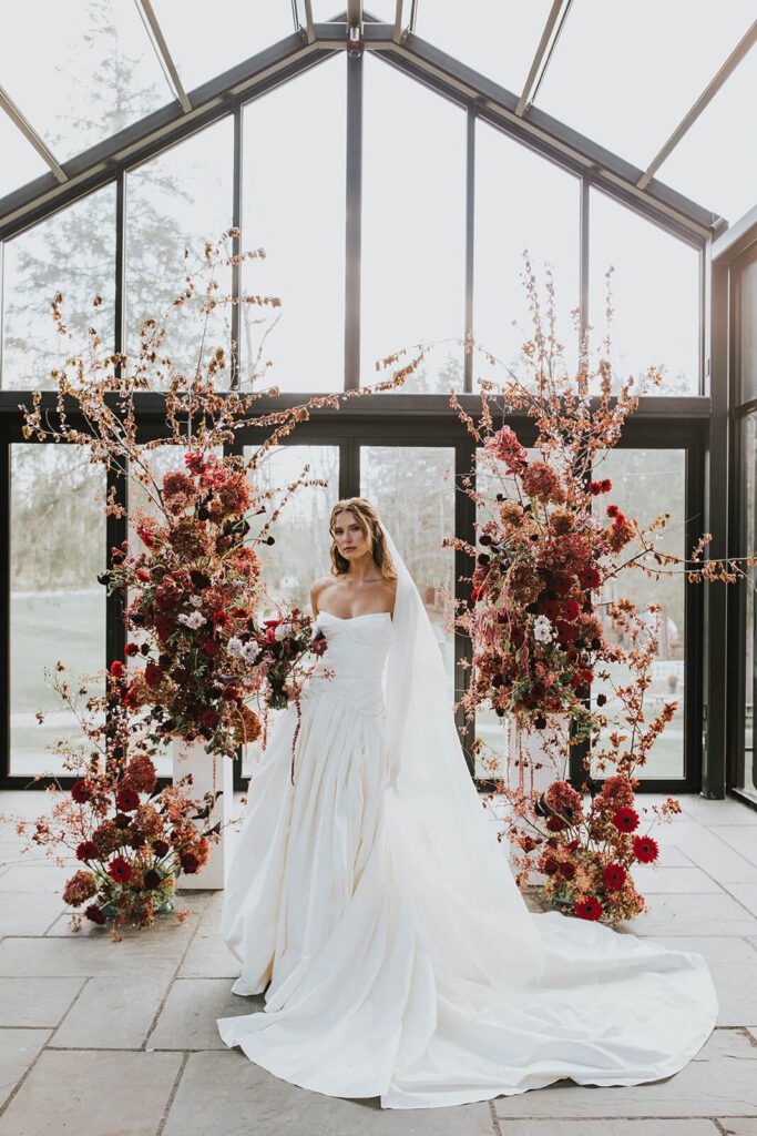 Bride wearing drop waist corseted wedding dress and holding a romantic bouquet in shades of red