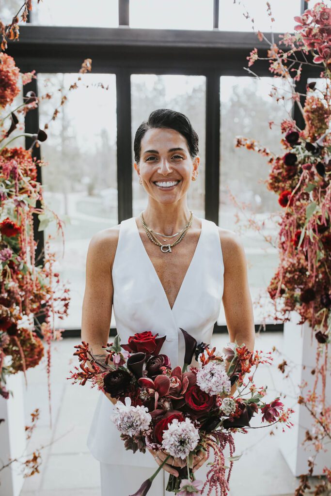 Bride wearing modern sleeveless suit and holding a romantic bouquet in shades of red