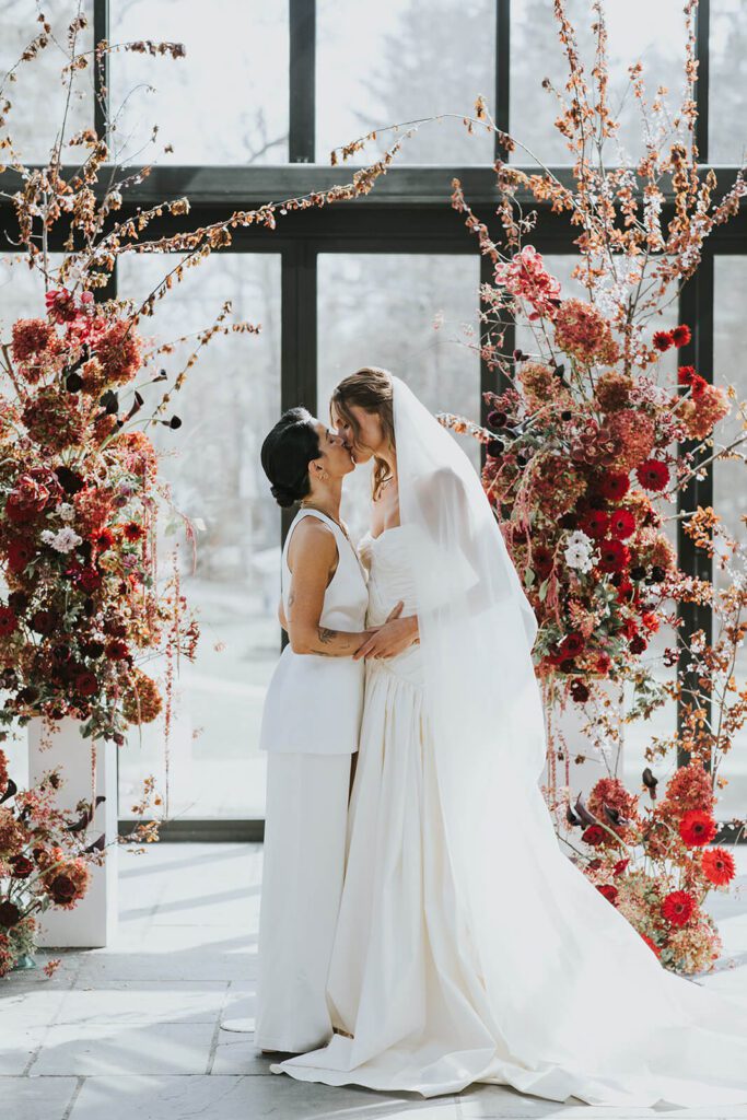 Two brides kissing during their wedding ceremony in the Glasshouse at Cedar Lakes Estate