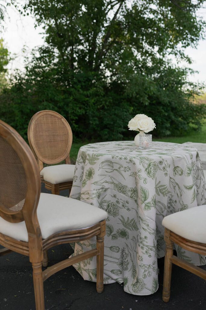 Cocktail hour table with a white and green tablecloth and elegant wooden chairs