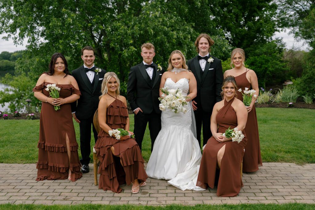Formal portrait of the wedding party with bridesmaids dressed in long brown dresses and groomsmen dressed in tuxedos