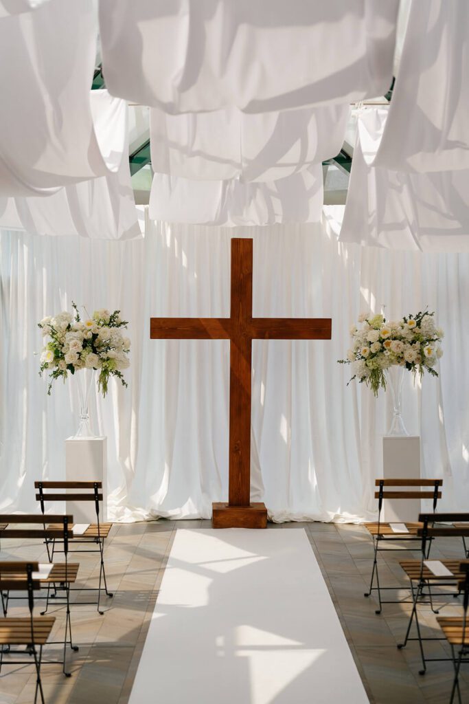Elegant white-draped wedding ceremony with a large wooden cross at The Montage Indianapolis