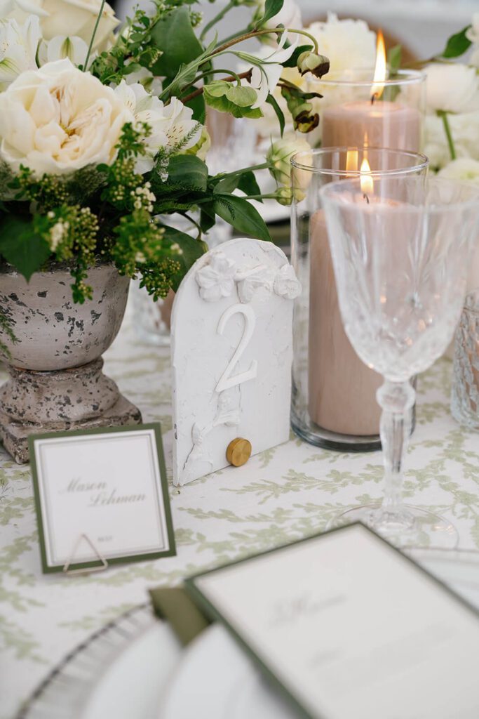 Elegant wedding table details including stone table number with floral details, green wedding menu, and green place card