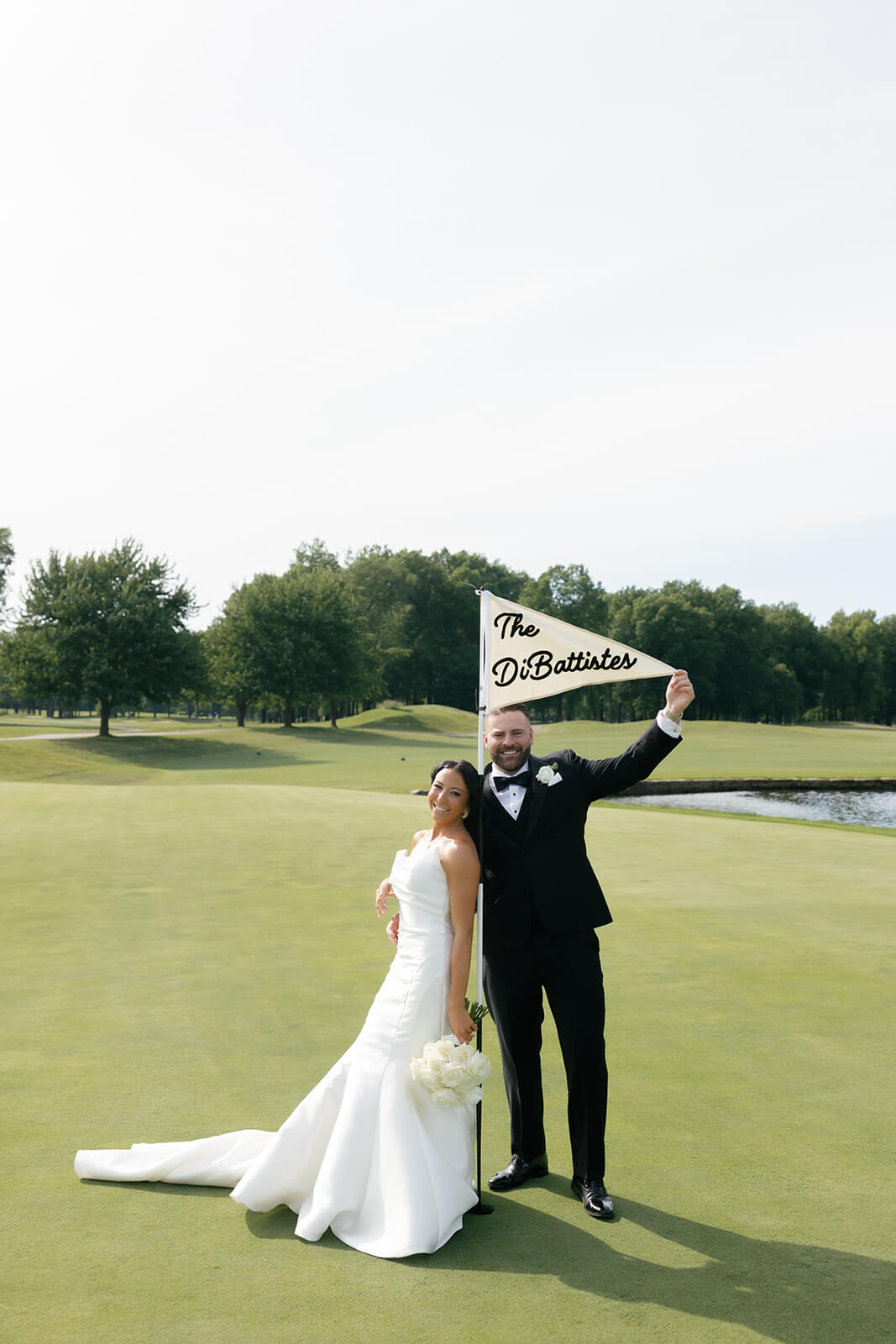 Bride and groom on a golf course posing by a custom golf flag with their last name