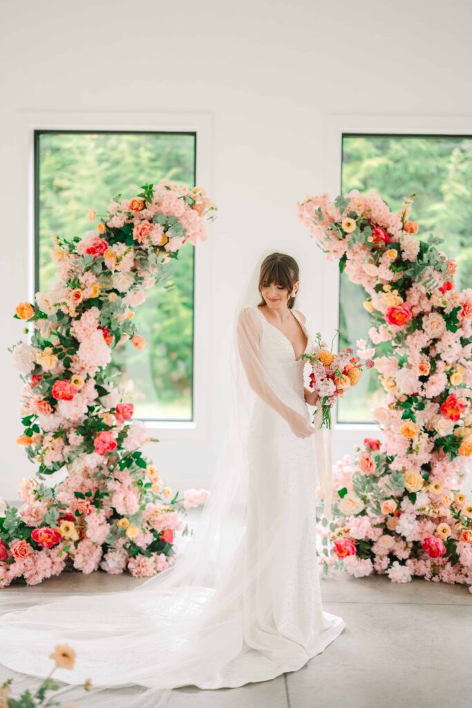 Portrait of a bride in front of her vibrant pink and peach floral wedding arch